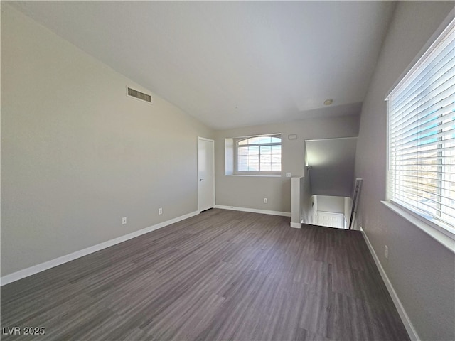 empty room featuring lofted ceiling, dark wood-style flooring, visible vents, and baseboards