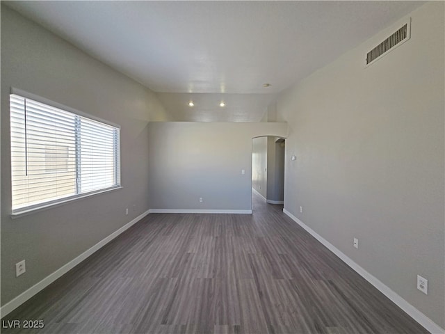 unfurnished room featuring baseboards, visible vents, vaulted ceiling, and dark wood-type flooring