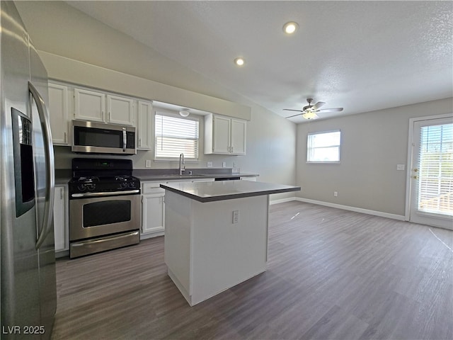 kitchen with appliances with stainless steel finishes, dark wood-type flooring, white cabinets, a sink, and a kitchen island