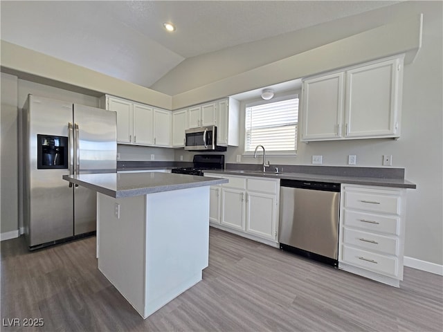 kitchen featuring stainless steel appliances, white cabinets, vaulted ceiling, and a sink