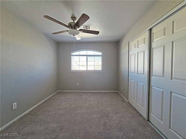 unfurnished bedroom with a closet, visible vents, carpet flooring, a textured ceiling, and baseboards