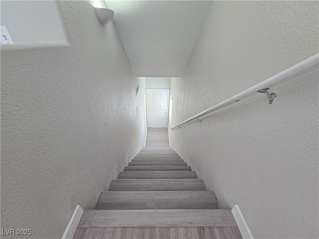 stairs with wood finished floors and a textured wall