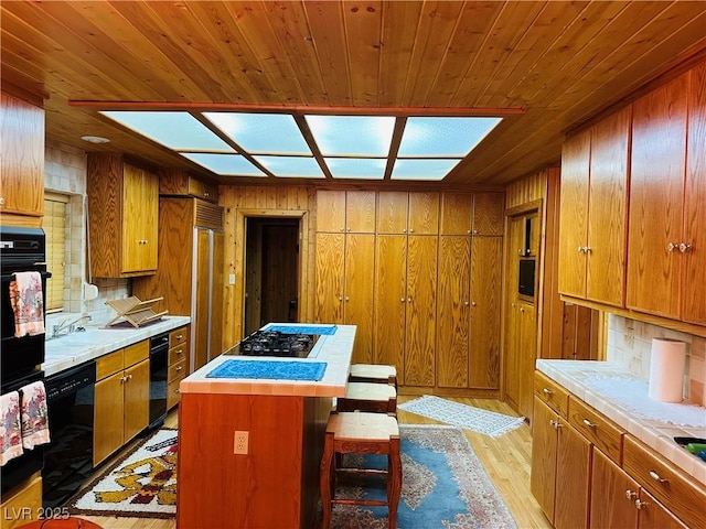 kitchen featuring black appliances, light wood finished floors, backsplash, and brown cabinets