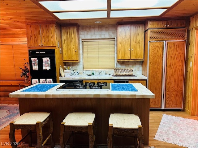 kitchen featuring tasteful backsplash, tile countertops, a breakfast bar area, light wood-style floors, and paneled fridge