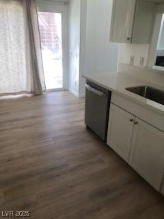 kitchen with light wood finished floors, light countertops, stainless steel dishwasher, white cabinetry, and a sink