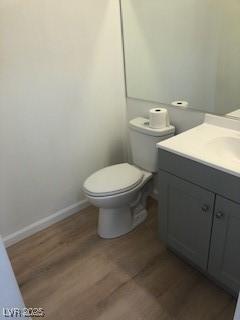 half bathroom featuring wood finished floors, vanity, toilet, and baseboards