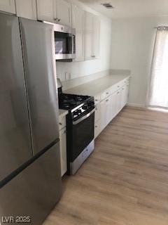 kitchen featuring appliances with stainless steel finishes, light countertops, light wood finished floors, and white cabinetry