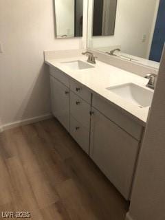 full bathroom with double vanity, wood finished floors, a sink, and baseboards