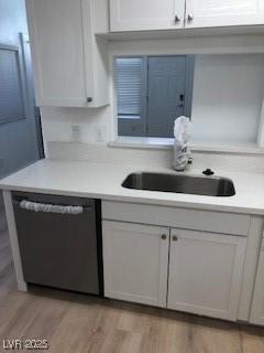 kitchen featuring light countertops, stainless steel dishwasher, light wood-style floors, white cabinets, and a sink