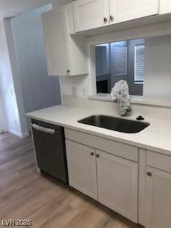 kitchen featuring dishwashing machine, a sink, white cabinetry, light countertops, and light wood finished floors