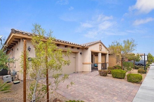 view of front of house with cooling unit, a garage, a tiled roof, decorative driveway, and stucco siding