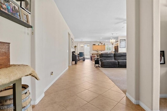 hallway with light tile patterned flooring, baseboards, and an inviting chandelier