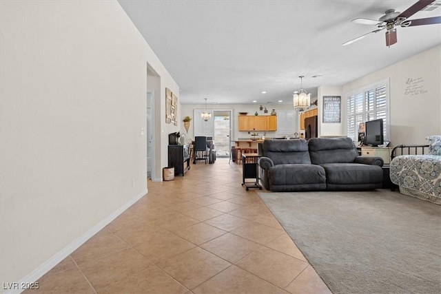 living area featuring ceiling fan with notable chandelier, plenty of natural light, light tile patterned flooring, and baseboards