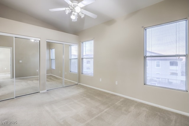 unfurnished bedroom with carpet, baseboards, vaulted ceiling, and two closets