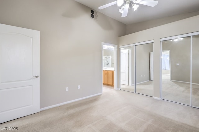 unfurnished bedroom with light carpet, baseboards, vaulted ceiling, multiple closets, and ensuite bath