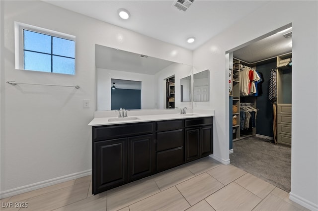 bathroom with double vanity, visible vents, a walk in closet, and a sink