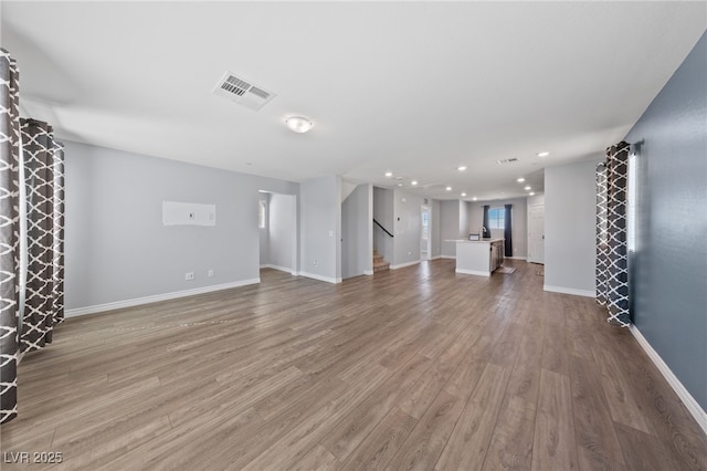 unfurnished living room with light wood finished floors, baseboards, visible vents, stairs, and recessed lighting