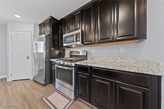 kitchen with stainless steel appliances, light stone counters, and light wood-type flooring