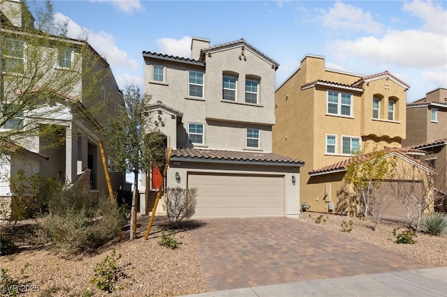 mediterranean / spanish house featuring a garage, a chimney, a tiled roof, decorative driveway, and stucco siding