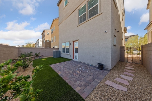 rear view of house with stucco siding, a gate, a patio area, central AC, and a fenced backyard