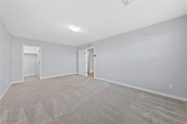 unfurnished bedroom featuring carpet, a walk in closet, visible vents, and baseboards