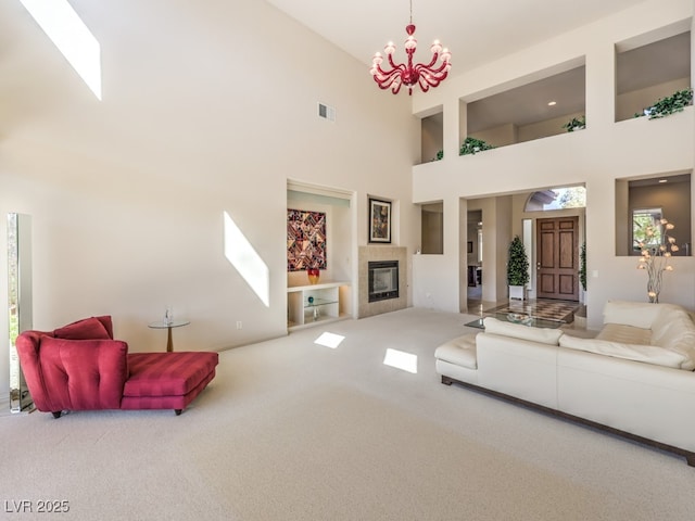 carpeted living area featuring an inviting chandelier, a high ceiling, visible vents, and a tiled fireplace