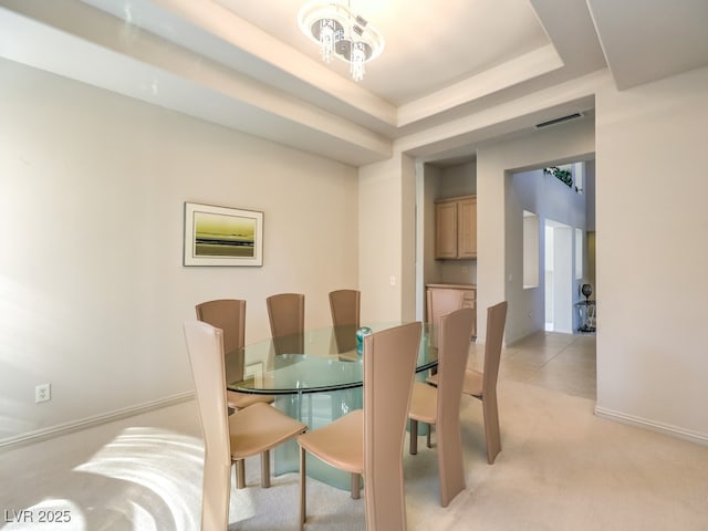 dining room with a tray ceiling, a notable chandelier, visible vents, light carpet, and baseboards