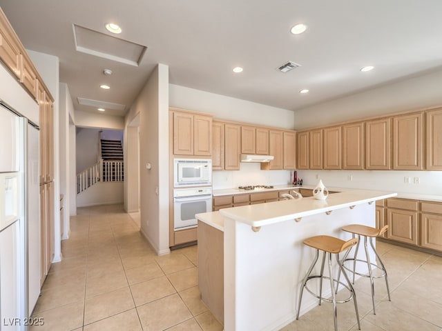 kitchen featuring light countertops, visible vents, light brown cabinets, white appliances, and under cabinet range hood