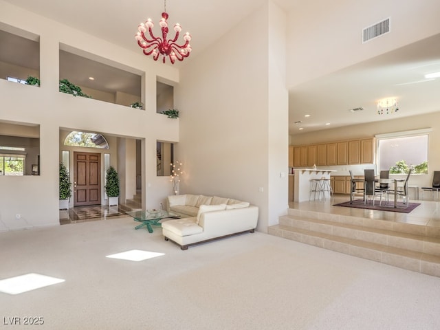 living room featuring an inviting chandelier, a towering ceiling, visible vents, recessed lighting, and carpet flooring