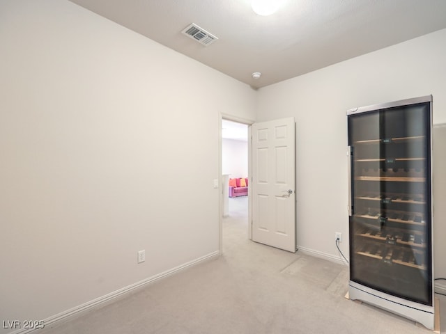 unfurnished bedroom with wine cooler, light colored carpet, baseboards, and visible vents