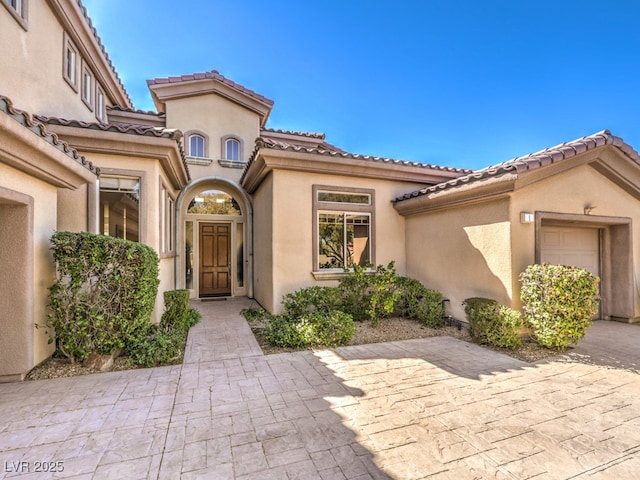 entrance to property with a tiled roof, a garage, and stucco siding