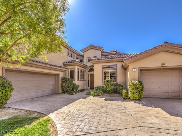 mediterranean / spanish-style house with a garage, stucco siding, decorative driveway, and a tile roof