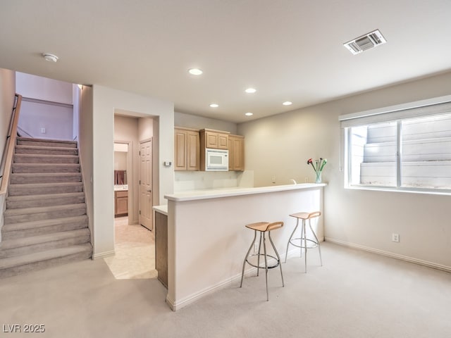 kitchen with visible vents, light colored carpet, white microwave, a breakfast bar, and light brown cabinets