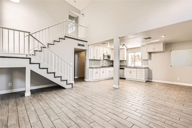 unfurnished living room featuring baseboards, visible vents, light wood-style flooring, stairway, and a sink