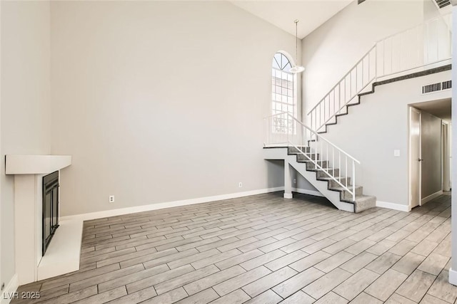 unfurnished living room with visible vents, wood finished floors, a towering ceiling, and baseboards