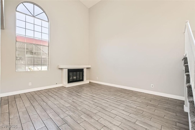 unfurnished living room with a glass covered fireplace, stairway, baseboards, and wood finished floors