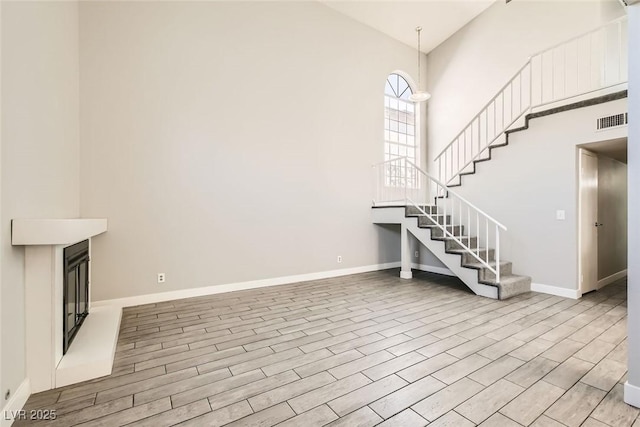 unfurnished living room with visible vents, baseboards, stairway, wood finished floors, and high vaulted ceiling