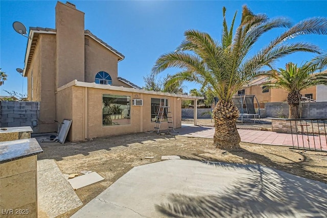 rear view of property with a chimney, a trampoline, fence, a patio area, and stucco siding