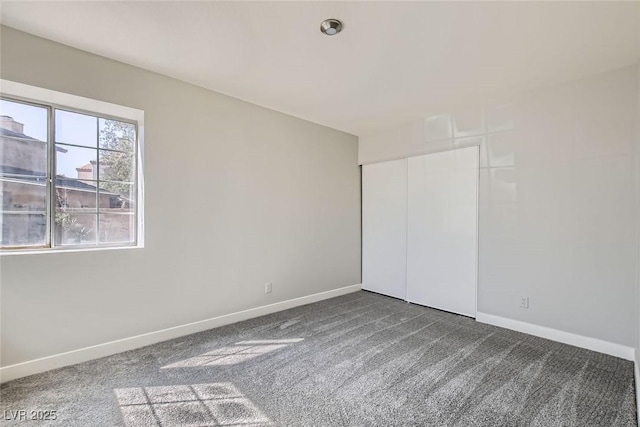 unfurnished bedroom with baseboards, dark carpet, and a closet