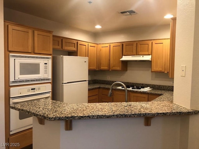 kitchen featuring visible vents, a peninsula, white appliances, under cabinet range hood, and a kitchen breakfast bar