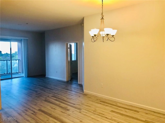 empty room featuring a chandelier, wood finished floors, and baseboards