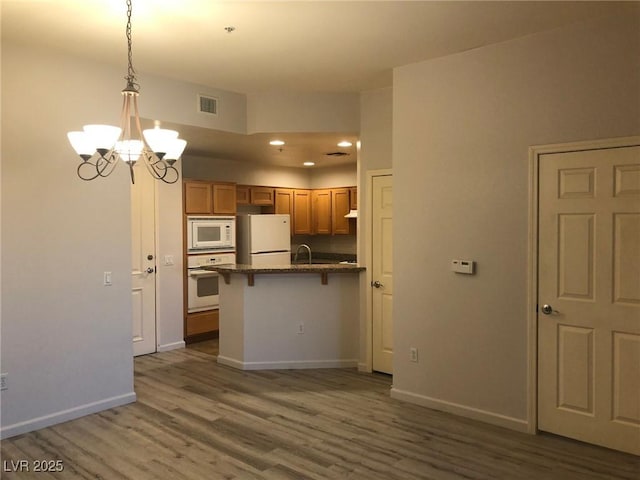 kitchen with visible vents, wood finished floors, white appliances, a peninsula, and a kitchen bar