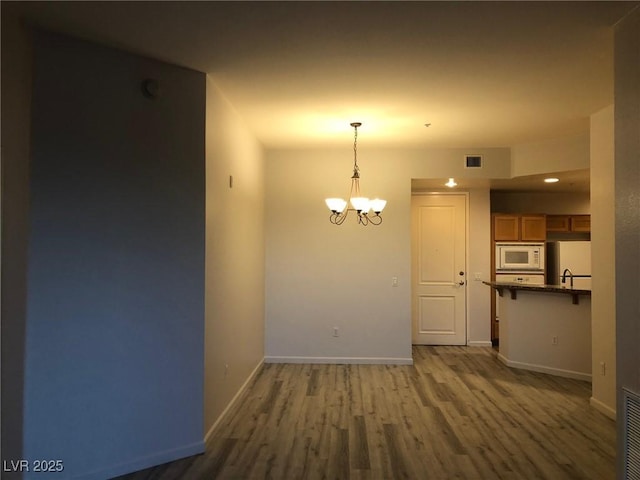 unfurnished dining area with a notable chandelier, wood finished floors, visible vents, and baseboards