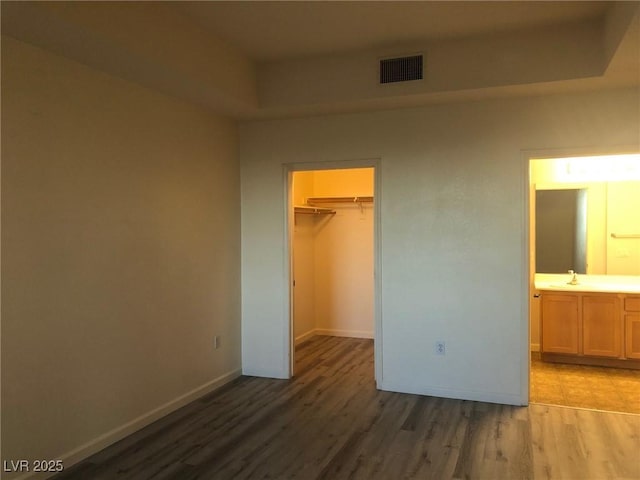 unfurnished bedroom featuring baseboards, a spacious closet, visible vents, and wood finished floors