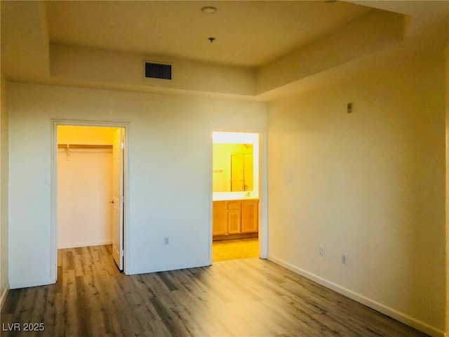 unfurnished bedroom featuring baseboards, visible vents, wood finished floors, a walk in closet, and a closet