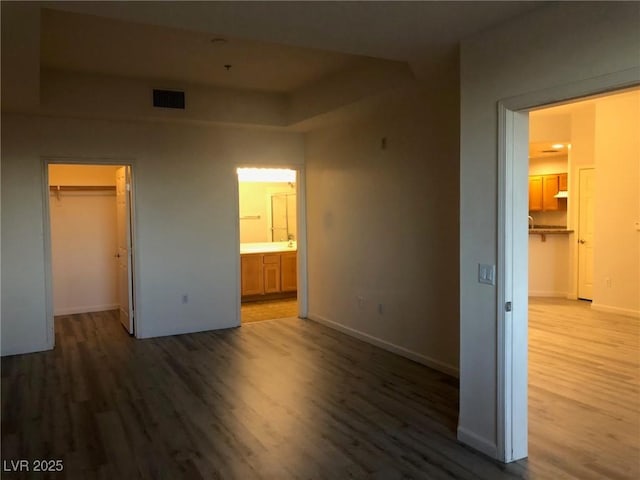 unfurnished bedroom with a walk in closet, a closet, baseboards, and wood finished floors