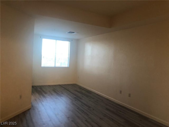 spare room with wood finished floors, visible vents, and baseboards