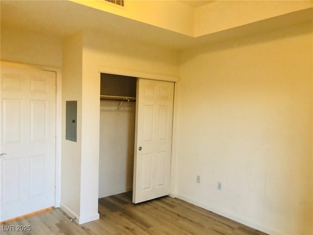 unfurnished bedroom with electric panel, a closet, baseboards, and wood finished floors