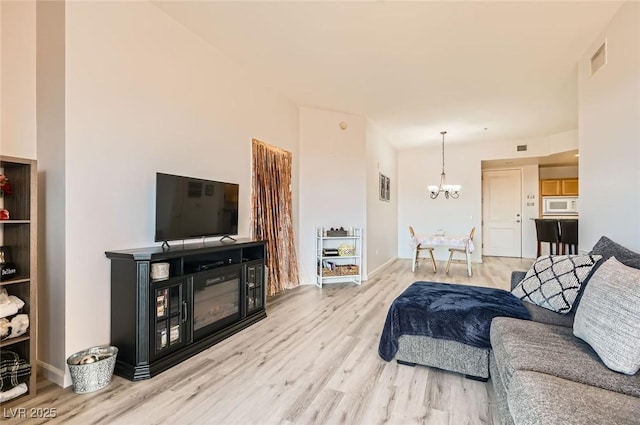 living area with baseboards, visible vents, wood finished floors, and a chandelier