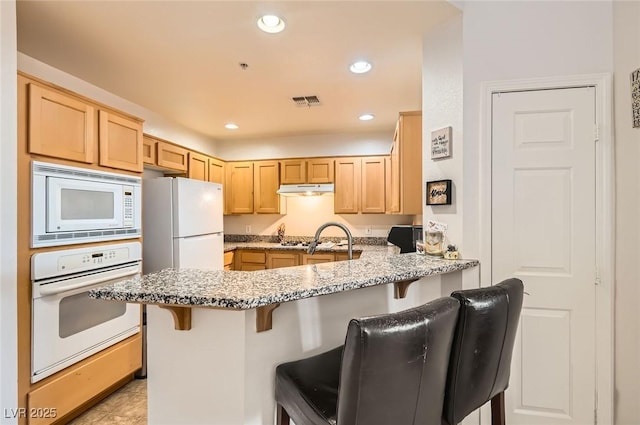 kitchen with recessed lighting, white appliances, under cabinet range hood, visible vents, and a peninsula